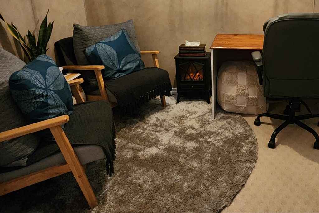 Comfortable client seating area in a softly lit counselling room, featuring warm tones, cushions, and a peaceful atmosphere that fosters safety and trust.