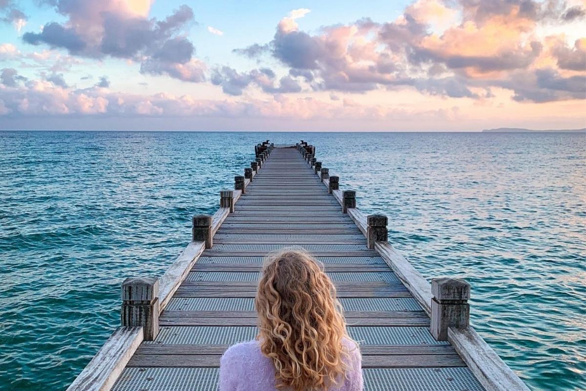 Counselling image of contemplation Woman sitting alone on a long wooden pier, gazing into the distance in quiet contemplation, symbolising a journey of self-discovery and emotional healing through counselling.